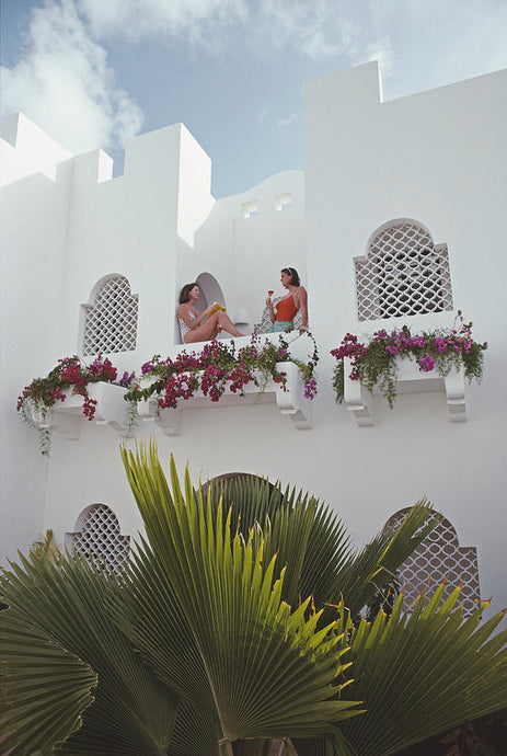 Cap Juluca Hotel by Slim Aarons - A photographic print of Patricia and Margaret O'Neil having a conversation on the balcony of the Cap Juluca Hotel.