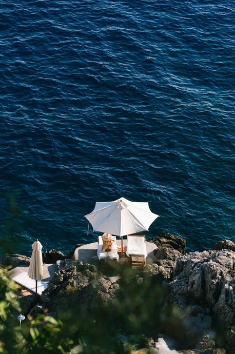 Casa Privata by Via Tolila - A photographic print capturing the coastal waters of Praiano, Italy, with a sun bather lounging under a crisp white umbrella.