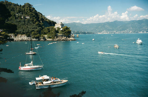 Castello Di Paraggi by Slim Aarons - Print of boats on a body of water with mountains in the background