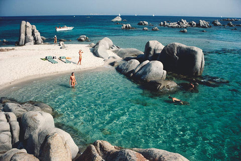 Cavallo Bathers by Slim Aarons - People enjoying the clear blue water near large rocks on a sunny day.
