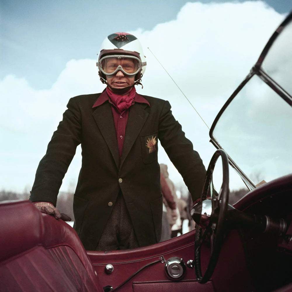 Gordon C MacKenzie by Slim Aarons - Person in vintage attire with helmet and goggles standing next to a classic car