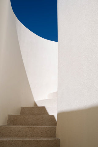 Greek Curves II by Via Tolila - A stunning photographic print of a curving staircase in Milos, Greece capturing the crisp white architecture against a clear blue sky.