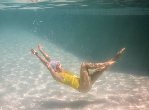 Halcyon Daze 1 by Francesca Owen - Underwater photography of a synchronised swimmer in yellow leotard and white cap posing underwater.