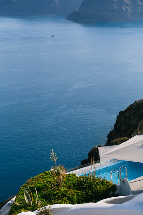 Hidden Pool by Via Tolila - A photographic print capturing a pool overlooking views of the brilliant blue water of Santorini, Greece.