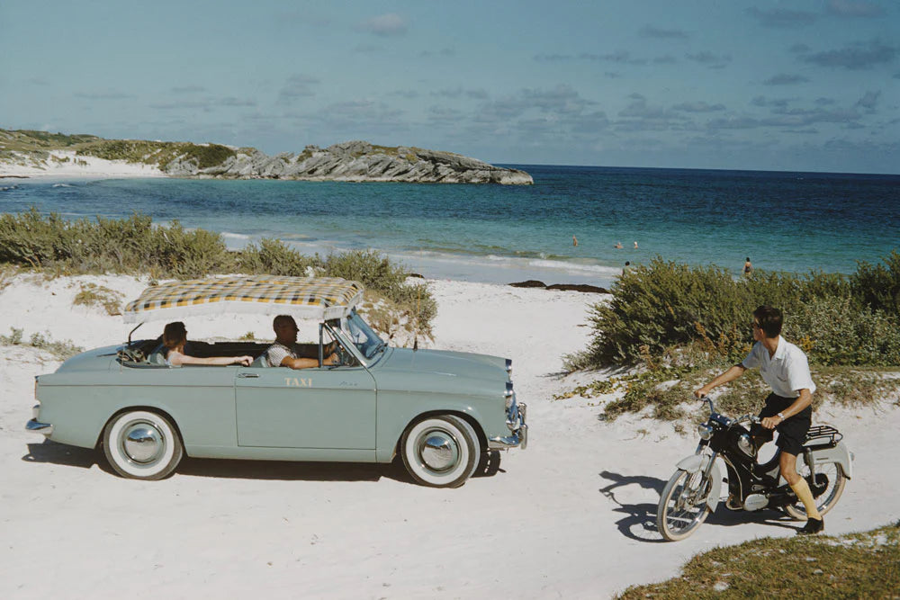 Horshoe Bay Bermuda by Slim Aarons - Vintage car and man on bicycle by the sea