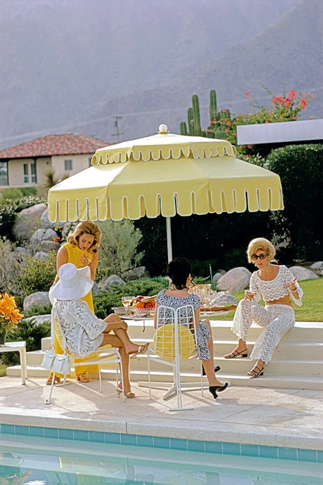 Palm Springs Life by Slim Aarons - Fashionable ladies gathered beneath a poolside vintage yellow umbrella.