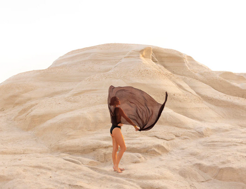 Signature Series - Mornings in Milos 05 by Francesca Owen - A contemporary image of a windswept sheath wavering around a female form in the sand rocks of Milos.