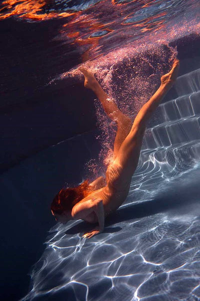 Signature Series - Glisten 03 - A photographic art print of a woman diving into a swimming pool, viewed from under the water.