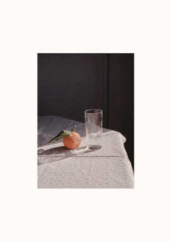 Sunrise by The Poster Club - An analoque film photograph of a breakfast table with a glass of water and an orange in the morning sunlight.