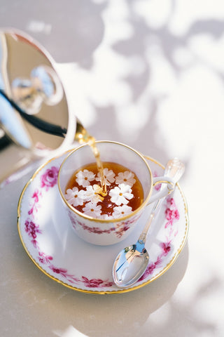 Tea Time in Versailles by Via Tolila - A photograph of an elegant tea cup and saucer with flowers in the herbal tea.