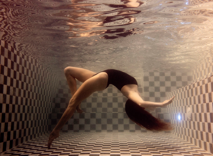 The Banya by Francesca Owen - Underwater photography of an artistic swimmer in black bathers posing in a black and white checkered tile pool.