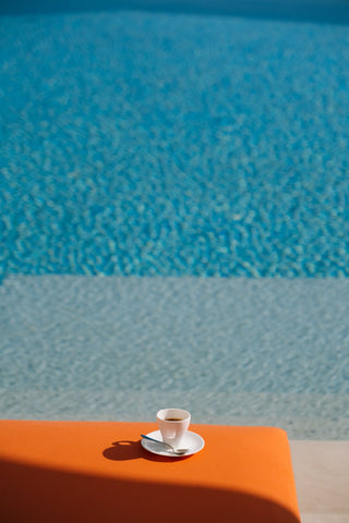 The Maybourne Riviera by Via Tolila - A photograph taken poolside of a coffee cup placed on an orange daybed.