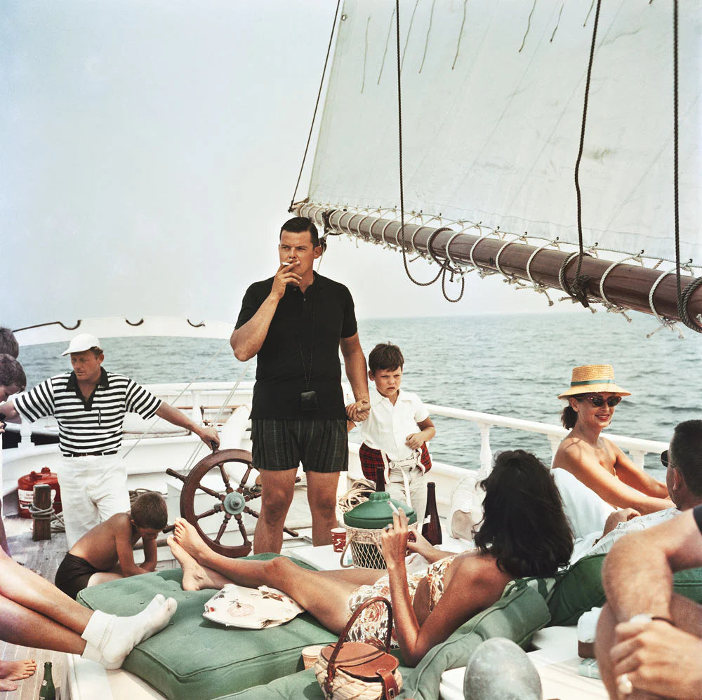 Black Pearl Trippers by Slim Aarons - Group of people on a sailboat with a man smoking a cigarette.