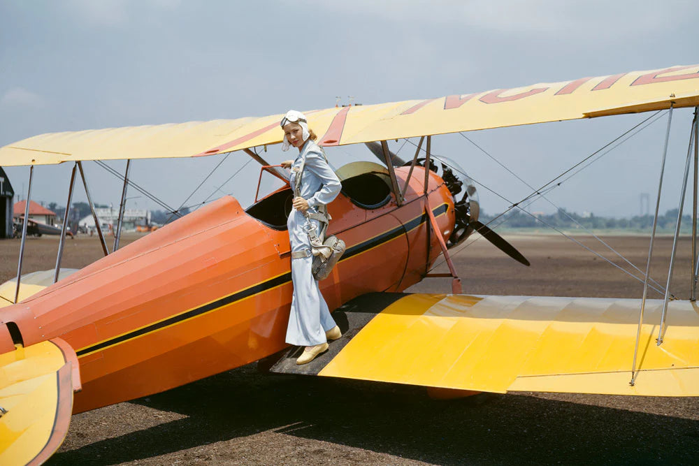 Female Pilot by Slim Aarons - Woman in vintage pilot outfit standing on wing of plane