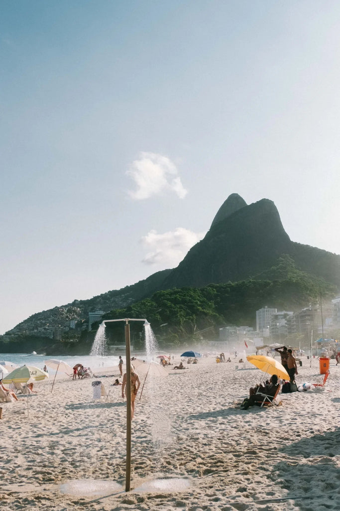 In THe Spirit of Rio by Via Tolila - Beach scene with people, umbrellas, and a mountain in the background