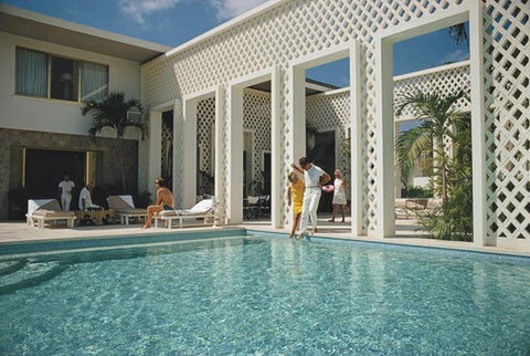 Arturo Pani’s Villa by Slim Aarons - A swimming pool at a white villa with two people dipping their toes in the water.