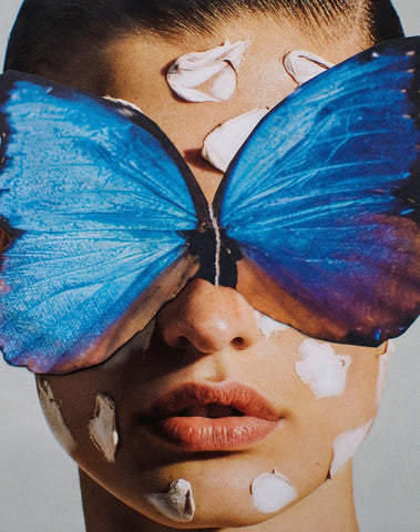 Broken Wings Blue by Dina Broadhurst - A close up photograph of a face, with vibrant blue butterfly wings collaged atop the figure's eyes. Her lips are slightly parted and she has flecks of paint or skincare on her face.