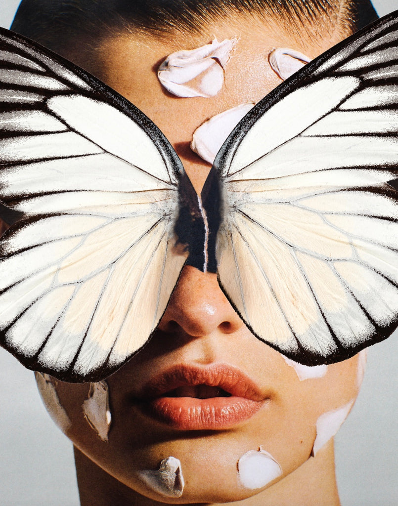 Broken Wings White by Dina Broadhurst - A close up photograph of a face, with white butterfly wings collaged atop the figure's eyes. Her lips are slightly parted and she has flecks of paint or skincare on her face.