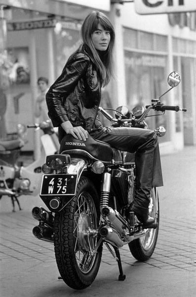Francoise Hardy by Getty Images (UK) Ltd - Black and white vintage photgraph of Francoise Hardy sitting on a motorbike looking back at the camera. She wears flared leather pants and an open leather jacket