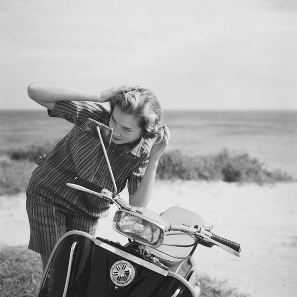 Holiday Hair Check by Getty Images (UK) Ltd - Vintage black and white photograph of a young lady checking her hair in the mirror of a motor scooter, Bermuda, 1958