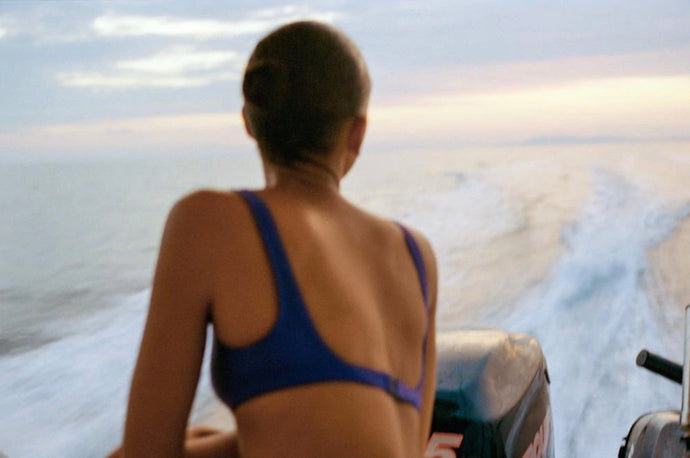 Looking Back by Akila Berjaoui. An out of focus film photograph of a girl in bikini top looking oiut over the water from the back of a boat.