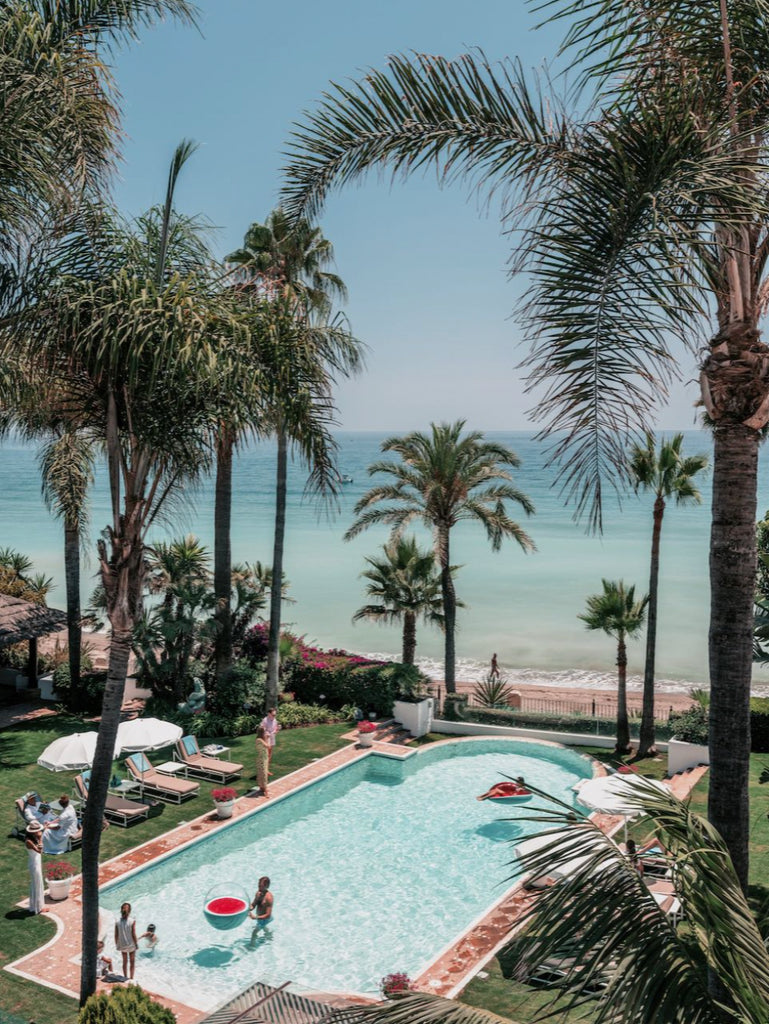 Marbella Club Days by Stuart Cantor - A photographic print of a beachside pool with the ocean in the background, surrounded by palm trees. 