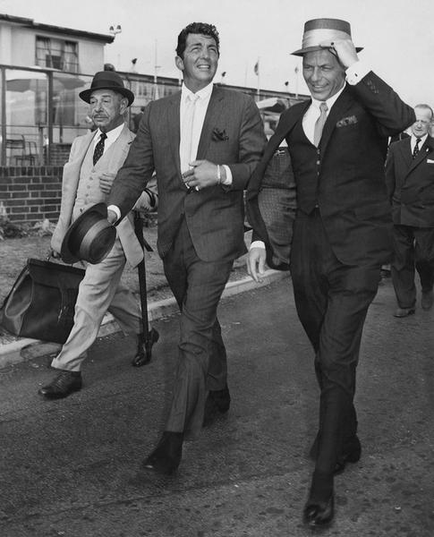 Martin And Sinatra by Getty Images (UK) Ltd - Black and white photograph of Dean Martin and Frank Sinatra looking dapper in suits and hats, arriving at London airport, with their friend Mike Romanoff