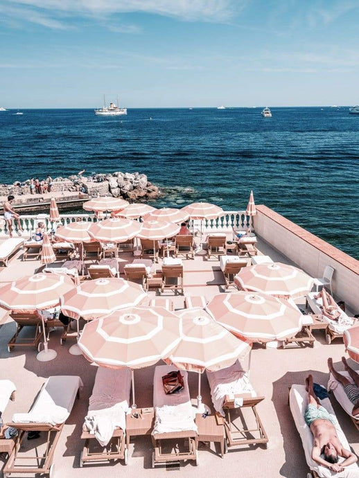 Old World Wonder by Stuart Cantor - Looking over the blue ocean, this photograph captures a rooftop scene of sunloungers with pale pink sun umbrellas from above