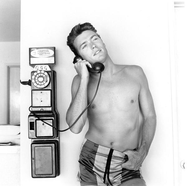 Pay Phone by Getty Images (UK) Ltd - A vintage black and white photograh of actor Clint Eastwood talking on a pay phone, wearing shorts