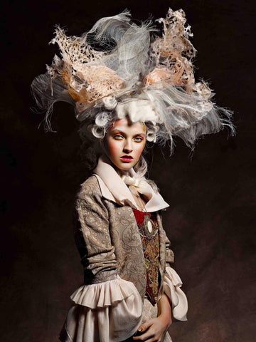 Renaissance 1 by Vincent Alvarez - A model dressed in renaissance fashion with wig looks to the camera. Her outfit is in soft blush tones and background is a dramatic dark brown.