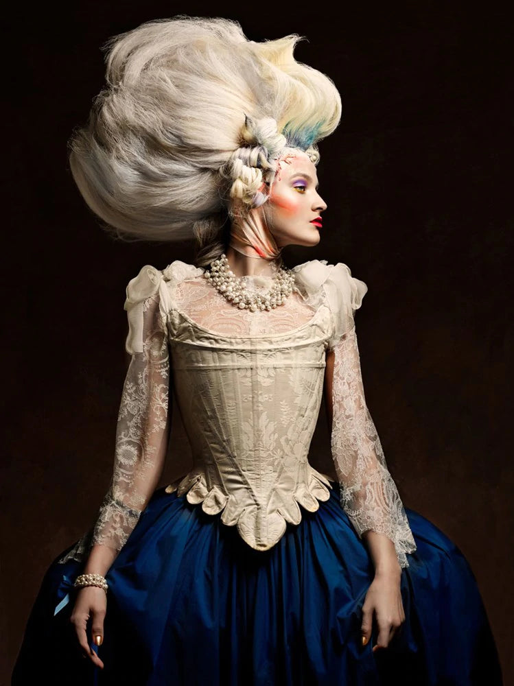 Renaissance 7 by Vincent Alvarez - A model in gown with navy blue skirt, tall white wig poses with side profile on a dramatic dark background 