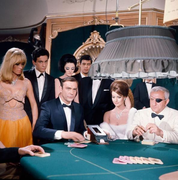 Sean Connery In Thunderball by Getty Images (UK) Ltd - Seated at a poker table, Sean Connery, as James Bond with Adolfo Celi as eye patch wearing Emilio Largo. Casino scene from the film 'Thunderball' in 1965. Glamorous onlookers in exquisite gowns and tuxedos
