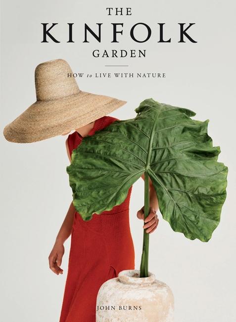 The Kinfolk Garden by John Burns - An artful image of a lady in red with straw hat placing a large green leaf in a rustic vase.