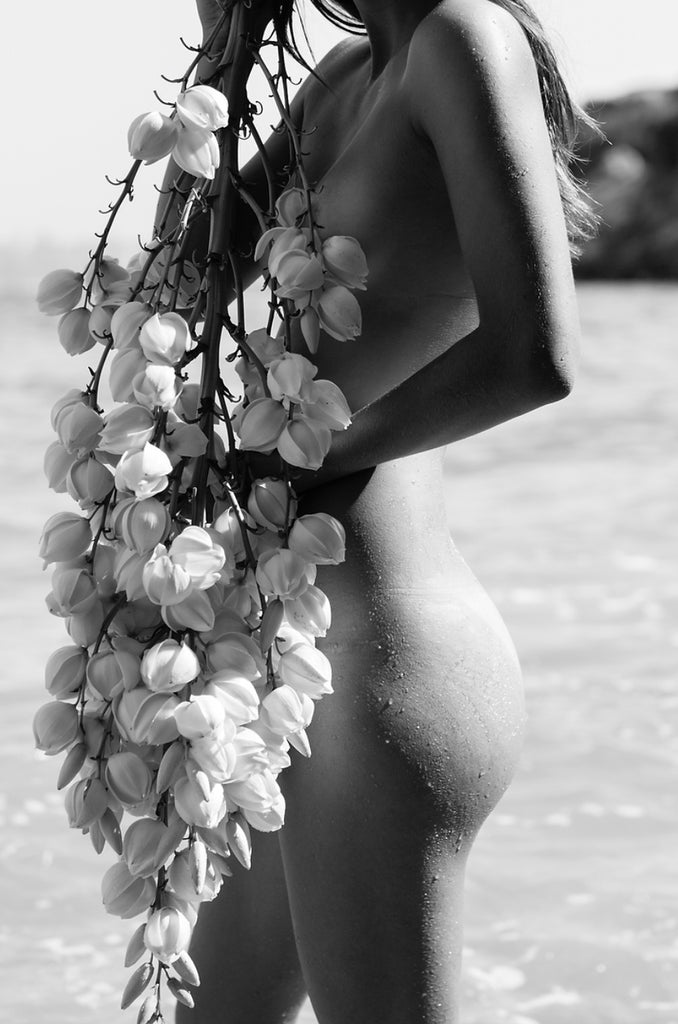 Under My Skin by Dina Broadhurst | FRAMING TO A T - A black and white portrait of a nude figure on the beach carrying a floral branch 