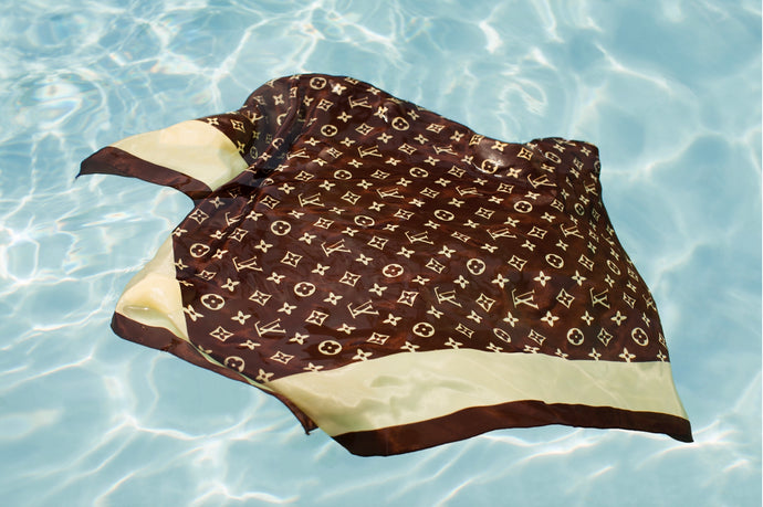 Underwater Love by Dina Broadhurst - A brown signature Louis Vuitton scarf floats, half-submerged in bright blue, crystal-clear water.