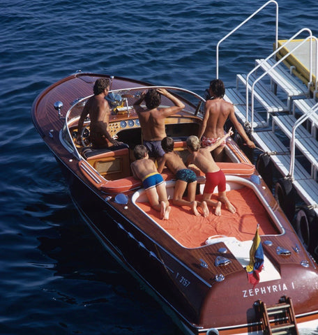 Zephyria by Slim Aarons - A photograph from 1970, holidaymakers aboard an elegant vintage burgundy speedboat.